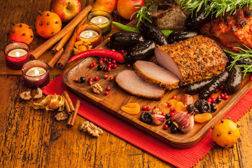 Christmas style meat selection of roasted pork and blood pudding with fruits and candles on rustic...