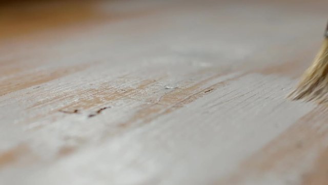 Applying white paint over wooden surface with a flat brush. Close up