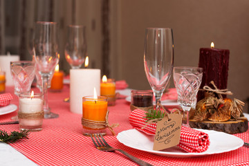 Festive composition with candles and plates. Table decoration. A beautiful table setting, red table cloth, tablecloth in the box. Christmas dinner. A Napkin decorated with inscription Merry Christmas
