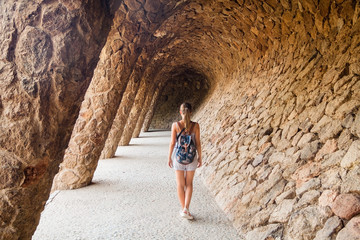 Young girl tourist with a backpack walking through the colonnade in Park Guell by architect Antoni Gaudi. Barcelona, Spain