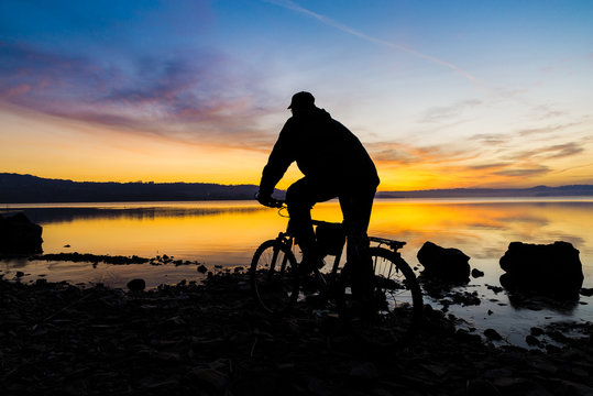 Silhouette of a mountain bike and of a cyclist at sunrise over the lake (lake Varese - Varese, Italy) - Focus on mountain bike and biker 