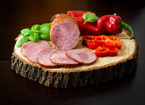 Sausage, ham with pepper and herbs on a wooden board, stump