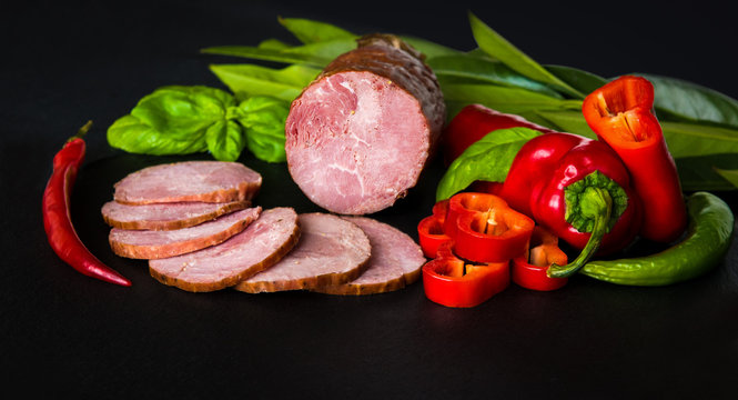 Sausage, ham with peppers and herbs on a dark background