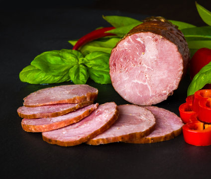 Sausage, ham with pepper and herbs on a dark background