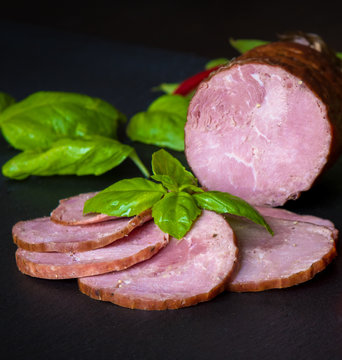 Sausage, ham with basil herbs on a dark background