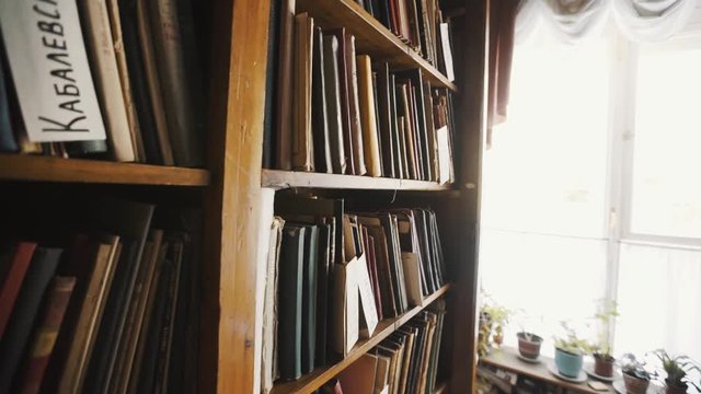 Dolly shot of bookshelves in old style library interior. Russian text, flowerpots
