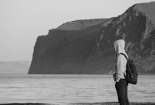 Человек в капюшоне у моря на фоне скал