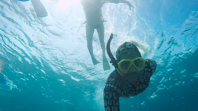 Couple of tourists in swimwear and flippers diving in the ocean near Bali island. Young woman is snorkelling near the water surface. Man in mask is exploring sea with underwater swimming.
