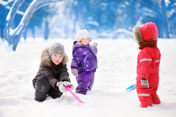 Little children in winter clothes having fun in park at the snowy winter day
