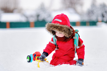 Little boy playing with bright car toy and fresh snow