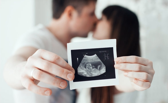 happy pregnant woman and man with ultrasound picture of baby