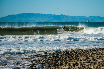 Surfer hitting lip as waves closes out with Santa Cruz Island in background.
