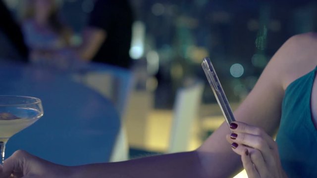 Young woman taking photo of cocktail with cellphone in bar at night
