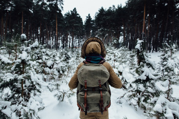 Woman in winter warm jacket with fur and rucksack walking in snowy winter pine forest