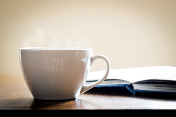 Cup of coffee and book on wooden table