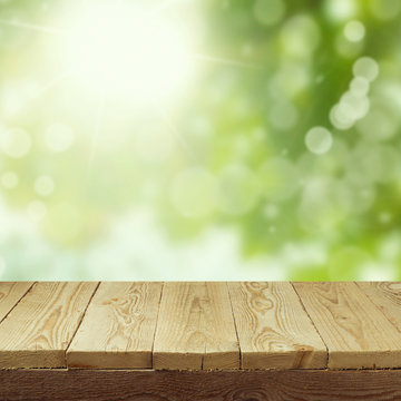 Empty wooden deck table with foliage bokeh background for product display montage. Spring or summer concept