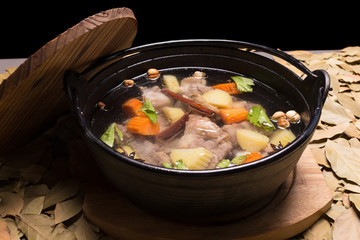 Clear oxtail soup on leaf background, black background.