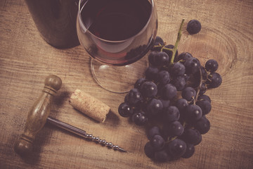 Glass of red wine with a sprig of grapes on a wooden table. - 134968390