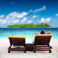 Woman on sunbed at tropical beach near green island