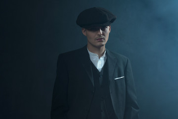 Retro 1920s english gangster wearing suit and flat cap standing