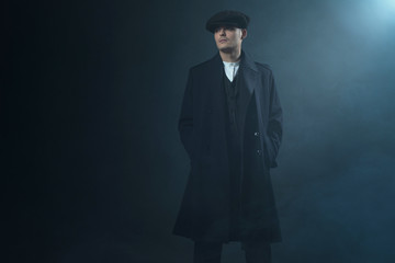 Retro 1920s english gangster wearing coat and flat cap standing