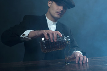 Retro 1920s english gangster with flat cap pouring whiskey. Peak - obrazy, fototapety, plakaty