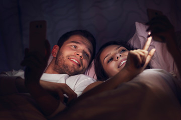 Young couple using smartphones in bed at night