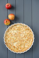 Apple tart with whole apples on grey stripped background