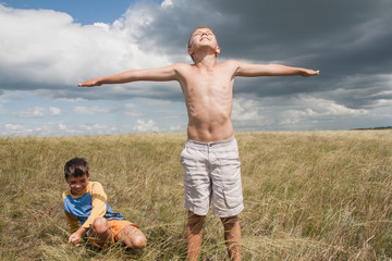 young boys playing in a field. boys in shorts. Boys stand in the desert. feather in the field. boy looking up at the sky. dreamer. two brothers. two friends. children playing in the field.