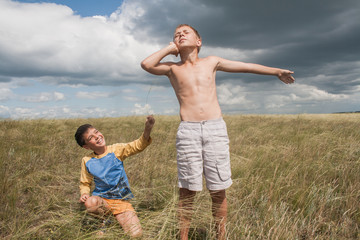 young boys playing in a field. boys in shorts. Boys stand in the desert. feather in the field. boy looking up at the sky. dreamer. two brothers. two friends. children playing in the field.