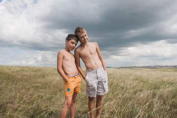 young boys standing in a field. boys in shorts. Boys stand in the desert. feather in the field. boy looking up at the sky. dreamer. two brothers. two friends. children playing in the field.