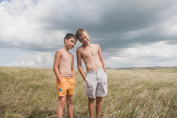 young boys standing in a field. boys in shorts. Boys stand in the desert. feather in the field. boy looking up at the sky. dreamer. two brothers. two friends. children playing in the field.