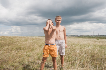young boys standing in a field. boys in shorts. Boys stand in the desert. feather in the field. boy looking up at the sky. dreamer. two brothers. two friends. children playing in the field.