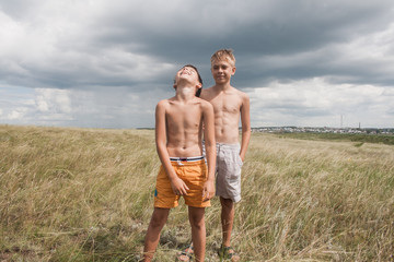 young boys standing in a field. boys in shorts. Boys stand in the desert. feather in the field. boy looking up at the sky. dreamer. two brothers. two friends. children playing in the field.