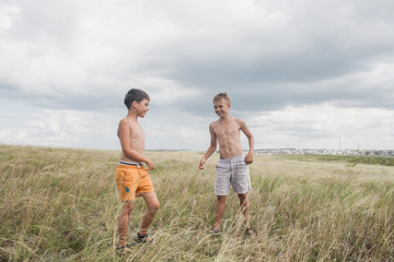 young boys standing in a field. boys in shorts. Boys stand in the desert. feather in the field. boy looking up at the sky. dreamer. two brothers. two friends. children playing in the field.