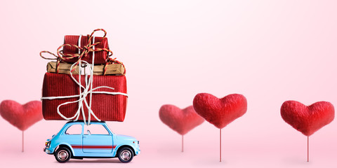 Blue retro toy car delivering gift box for Valentine's day on pink background with heart trees