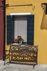 Red flower on the shattered window in the midst of yellow wall on Burano island, Venice