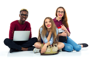 Three happy students sitting with books, laptop and bags