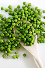 Isolated green peas on a wooden spoon against a white background