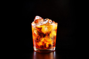 Glass of alcohol on a black table in the bar. Lonely scottish glass of whiskey with ice.