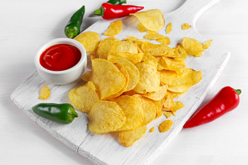 Gold and Crispy Potato Chips with hot sauce on white board, background.