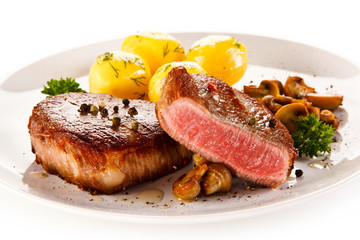 Grilled steaks, boiled potatoes and vegetable salad on white background 