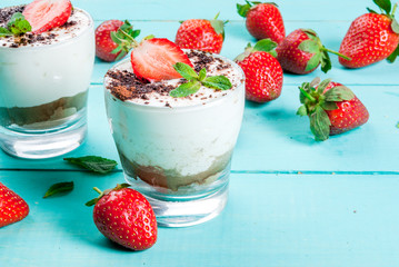 Summer dessert, classic cheesecake with strawberries decorated with mint leaves. On a light blue wooden table, bright sunlight. Copy space