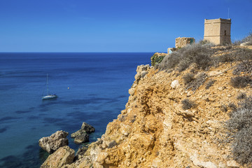 Fototapeta na wymiar Malta - Sail boat at Ghajn Tuffieha tower on a hot summer day with crystal clear blue sea water
