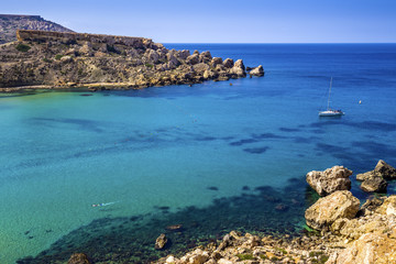 Malta - Snorkeling man and sail boat at Ghajn Tuffieha bay on a hot summer day with beautiful crystal clear sea water 
