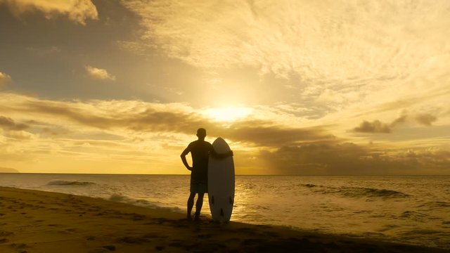 Young surfer on the beach waiting for perfect waves at sunset