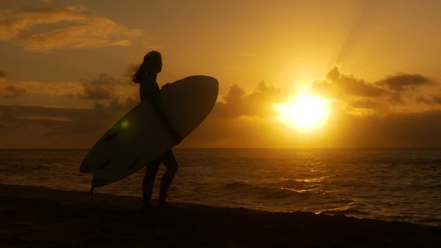 Young female surfer on the beach waiting for perfect waves at sunset