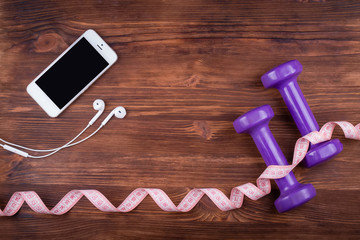 Wooden dark table with a phone, headphones, and dumbbells. Top v