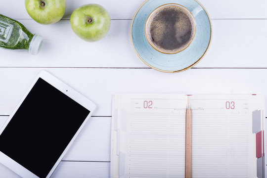 White wooden table with a tablet, notebook, detox and green appl