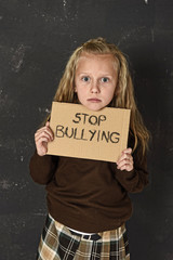 young little cute schoolgirl scared and sad asking for help showing message  with stop bullying text